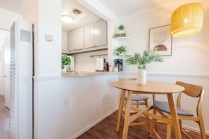 Eine moderne Küche mit weißen Schränken, ein Essbereich mit einem Holztisch und Stühlen sowie eine hängende Leuchte.