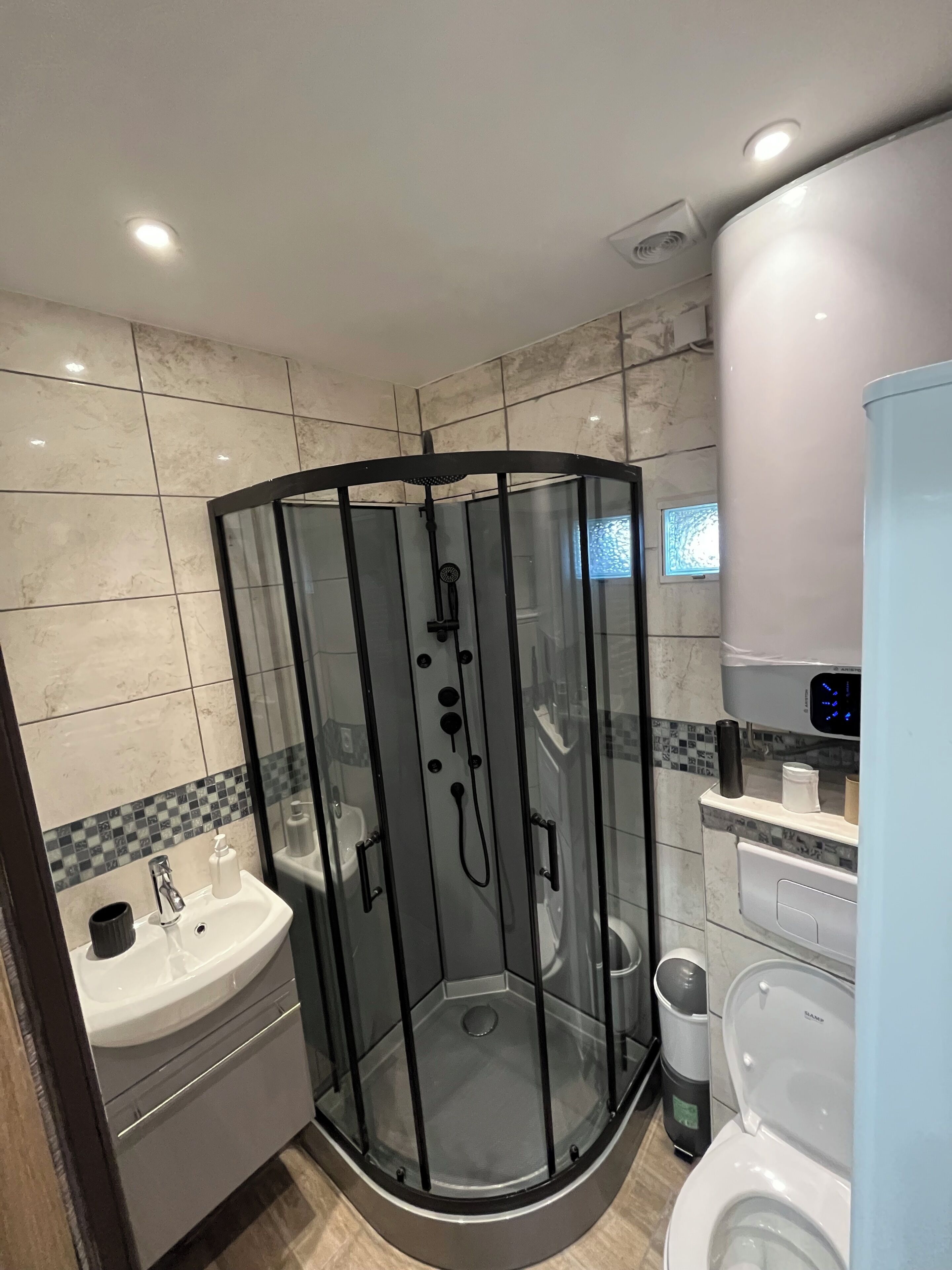 Une salle de bain moderne avec une douche à parois de verre, un lavabo, des toilettes et une poubelle.