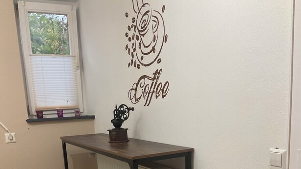 A small kitchenette with a coffee-themed wall decal, a radiator, and two stools.