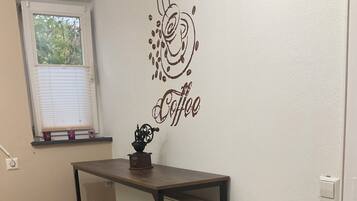 Une petite kitchenette avec un autocollant décoratif sur le mur sur le thème du café, un radiateur et deux tabourets.