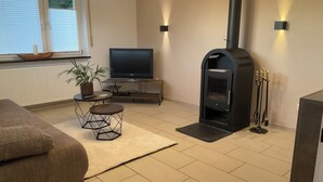 Ein Wohnzimmer mit einer Couch, einem Fernseher, einem Kamin und einem Esstisch mit Stühlen.