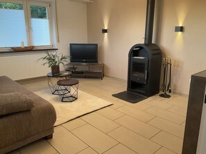 A living room with a sofa, a TV, a fireplace, and a dining table with chairs. - Waldglück Vacation Rental (Herrischried)
