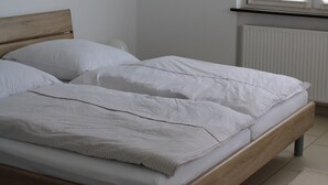 A bedroom with a wooden bed, white bedding, a radiator, and a window with blinds.