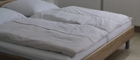 A bedroom with a wooden bed, white bedding, a radiator, and a window with blinds.