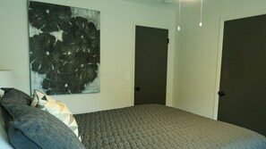 A bedroom with a bed, pillows, a wall-mounted abstract painting, and two closed doors. - Welcome to Southern ReBelle! Walk to campus for game days or relax by the pool (Oxford)