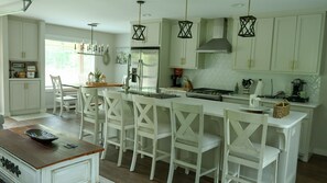 Una cocina con armarios blancos, una isla central con taburetes de bar, una estufa y una lámpara colgante.