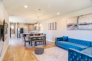 Ein modernes Wohnzimmer mit einem blauen Sofa, einem Essbereich mit Tisch und Stühlen sowie einer Küche im Hintergrund.