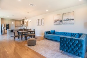 A modern living room with a blue sofa, a dining area with a table and chairs, and a kitchen in the background. - Luxury Stay Townhome in North Austin (Austin)