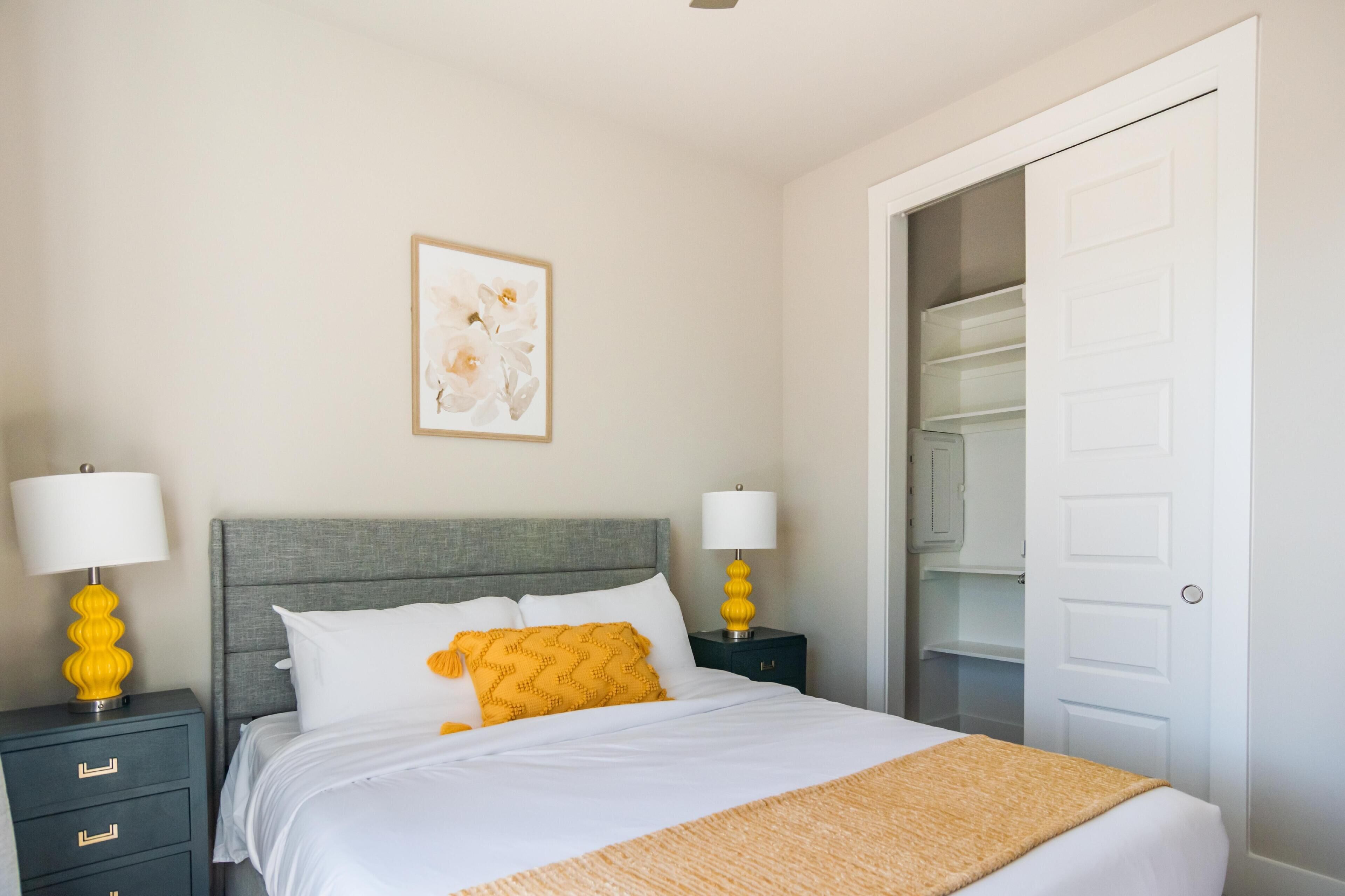 A bedroom with a bed, two bedside tables with lamps, a wardrobe, and a door to a closet.