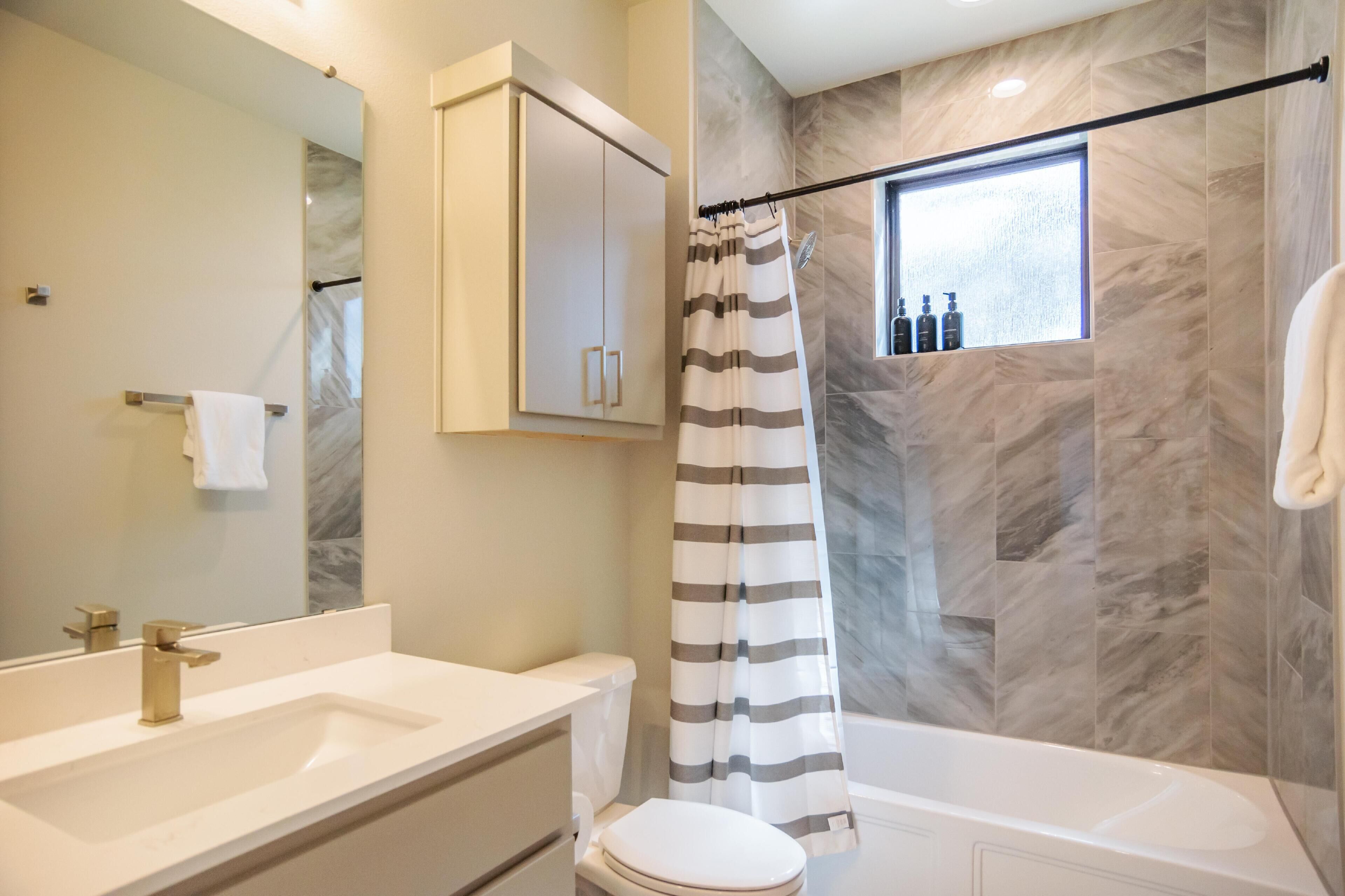 A bathroom with a marble wall, a bathtub, a toilet, a sink, and a shower curtain.