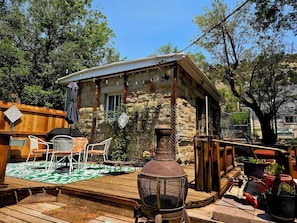Un edificio rústico de piedra con una terraza de madera, asientos exteriores y una parrilla metálica.