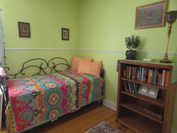 A room with a bed, a bookshelf, and two framed pictures on the wall.