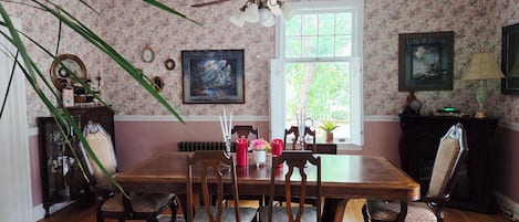 Une salle à manger avec une table en bois, des chaises, un lustre et un papier peint à motifs floraux.