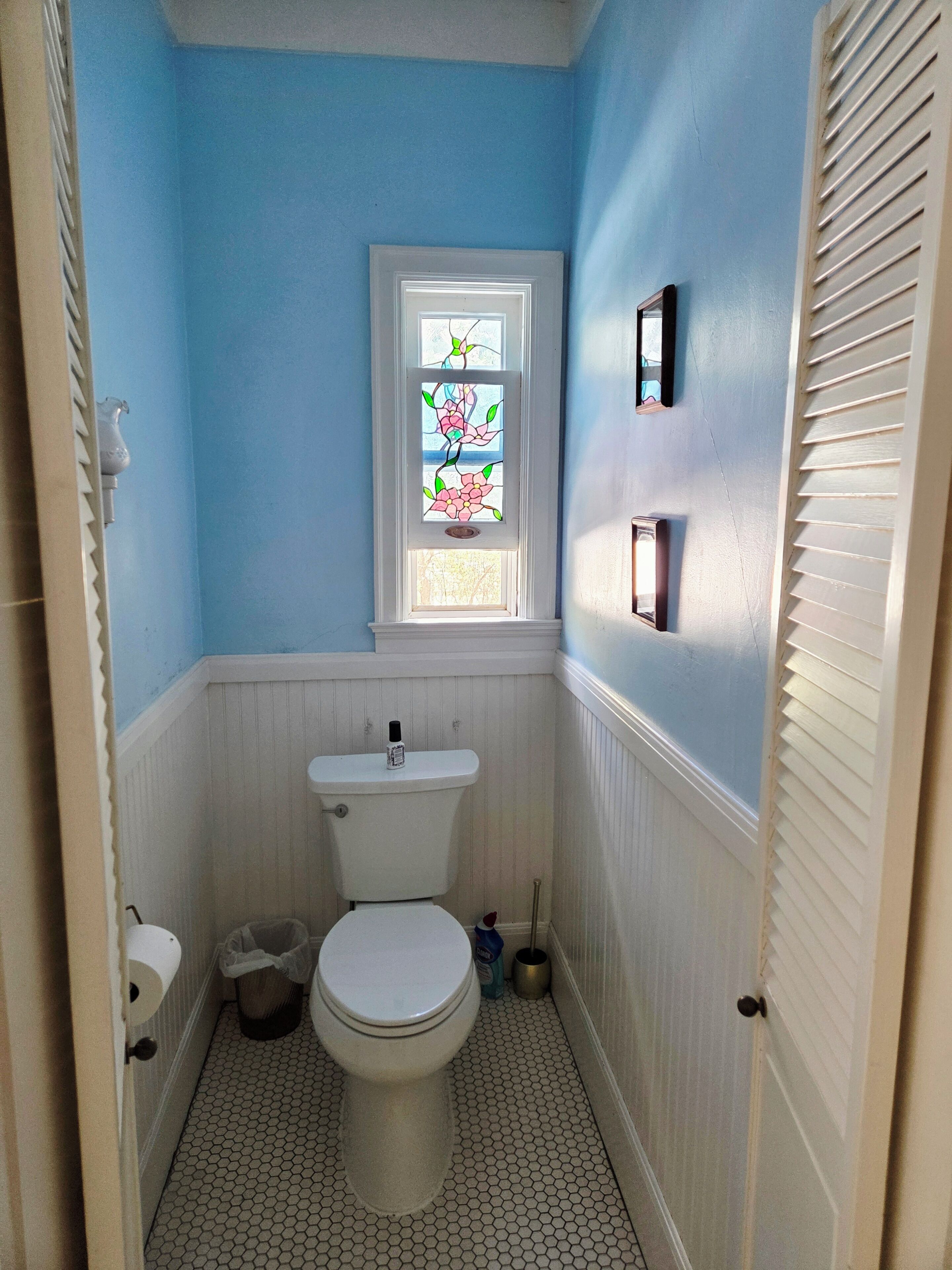 Une salle de bain avec des toilettes, une fenêtre ornée de vitraux et un lavabo blanc.