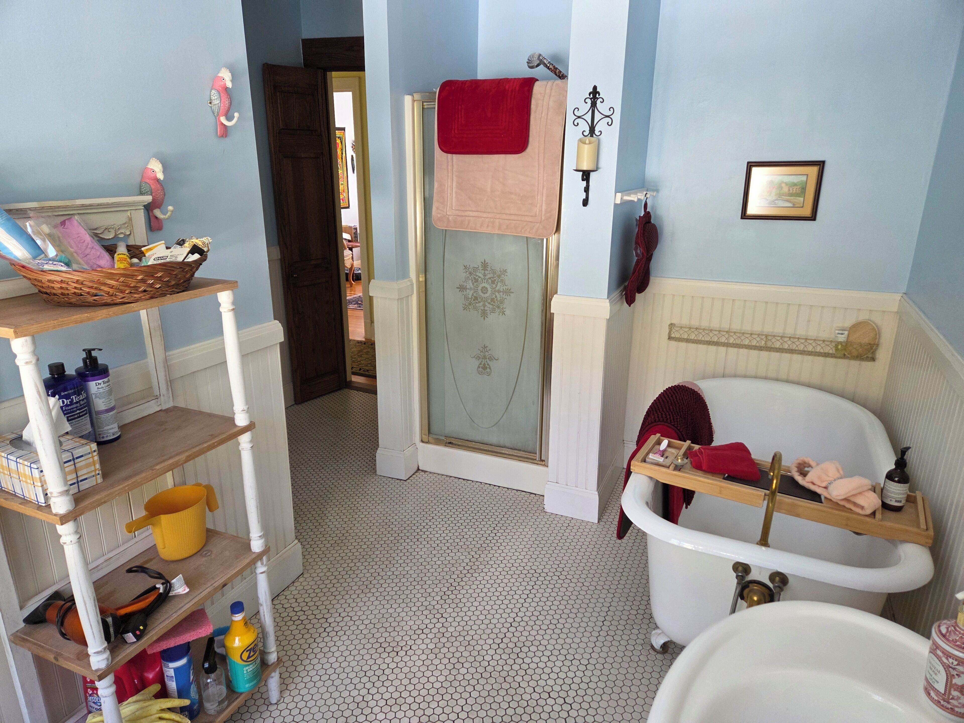 Un baño con bañera, ducha y lavabo. Hay repisas con artículos de aseo y una cesta a la izquierda.