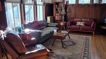 A spacious living room with a leather sofa, a red couch, and a wooden coffee table. Large windows allow natural light to fill the room.