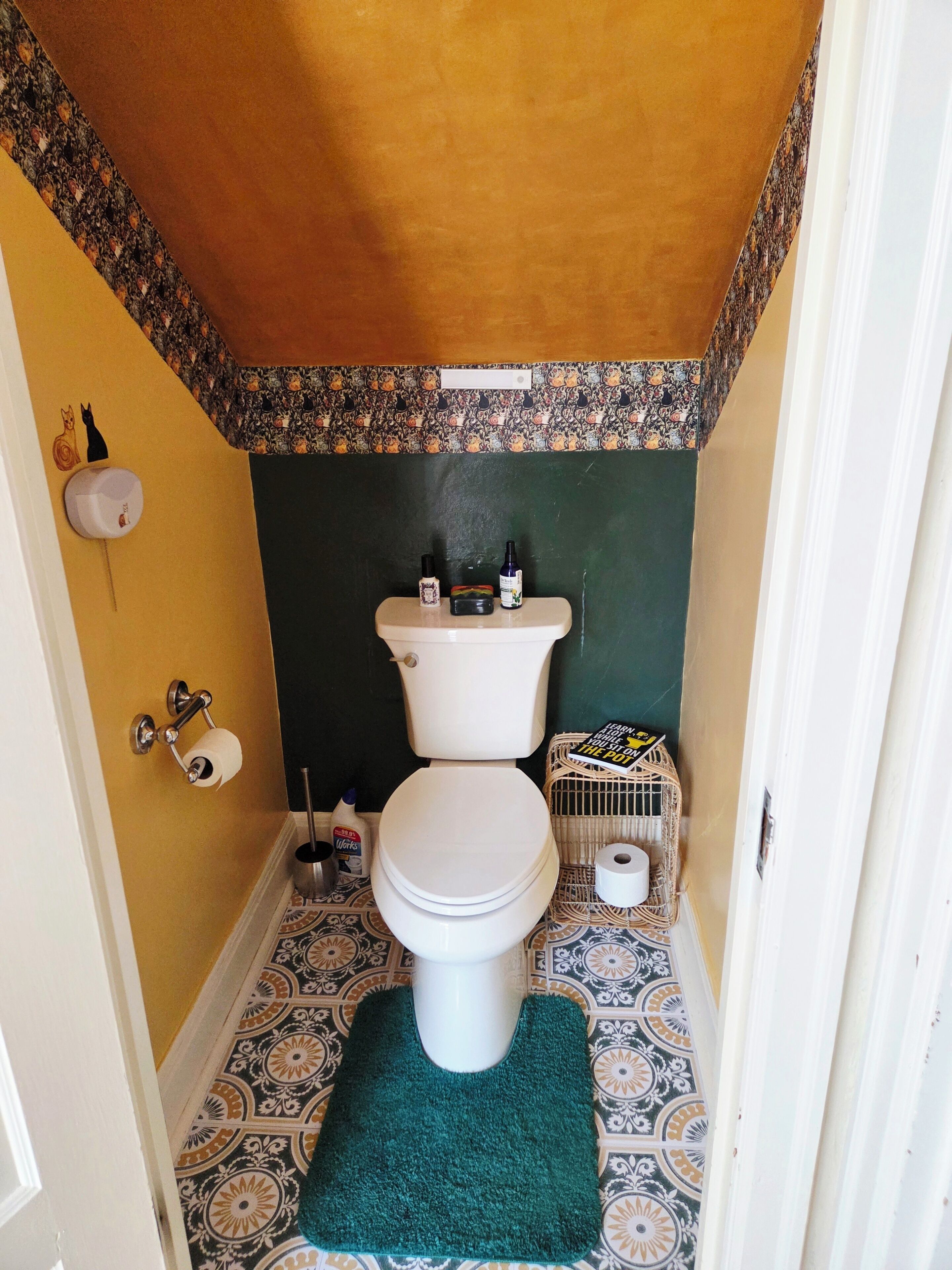 Een kleine badkamer met toilet, toiletpapierhouder, handzeepflesje en een klein mandje.