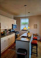 Cocina con armarios blancos, microondas, estufa y una isla grande con taburetes.