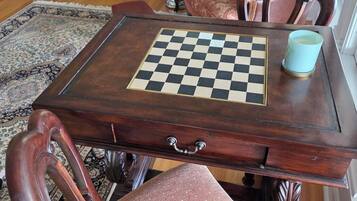 A wooden chess table with a checkered board, a light blue cup, and a patterned rug.