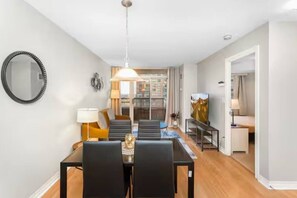A modern living room with a dining area, a large mirror, and a painting on the wall. - High-Rise Skyline Suite | Sleeps 5 | SQ1 (Mississauga)