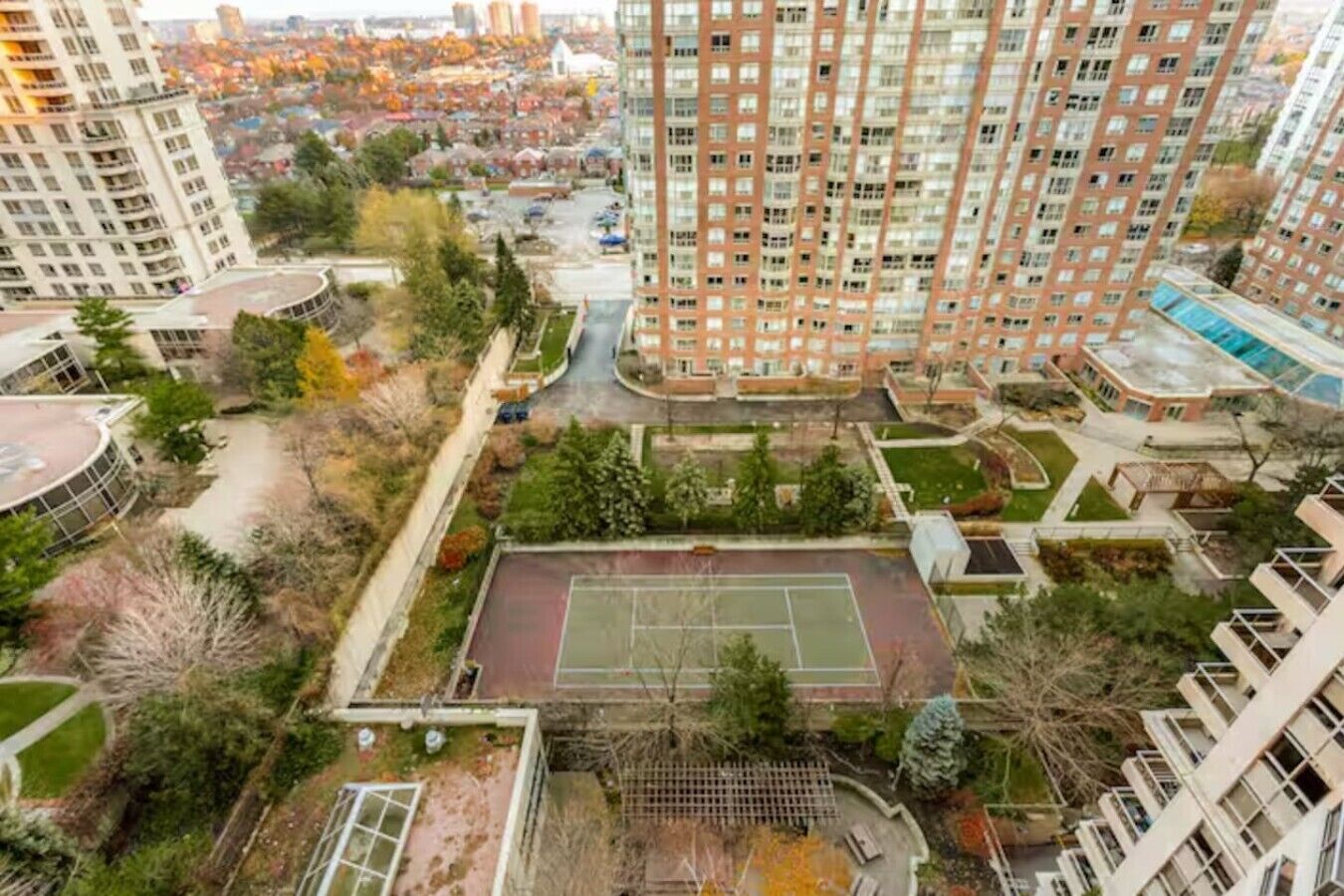 Ein Hochhaus mit Wohnungen und mehreren Balkonen, einem Tennisplatz und umliegender Bepflanzung.