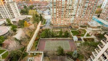 A high-rise residential building with multiple balconies, a tennis court, and surrounding greenery.