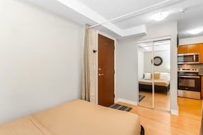 A bedroom with a bed, a door leading to a bathroom, and a kitchenette with an oven and microwave. - High-Rise Skyline Suite | Sleeps 5 | SQ1 (Mississauga)