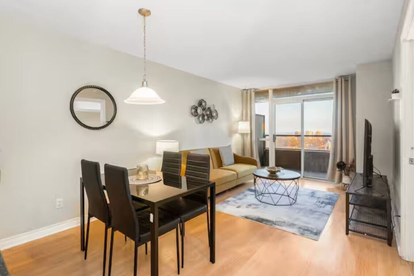 A modern living room with a dining area, a sofa, a TV, and a balcony with a view.