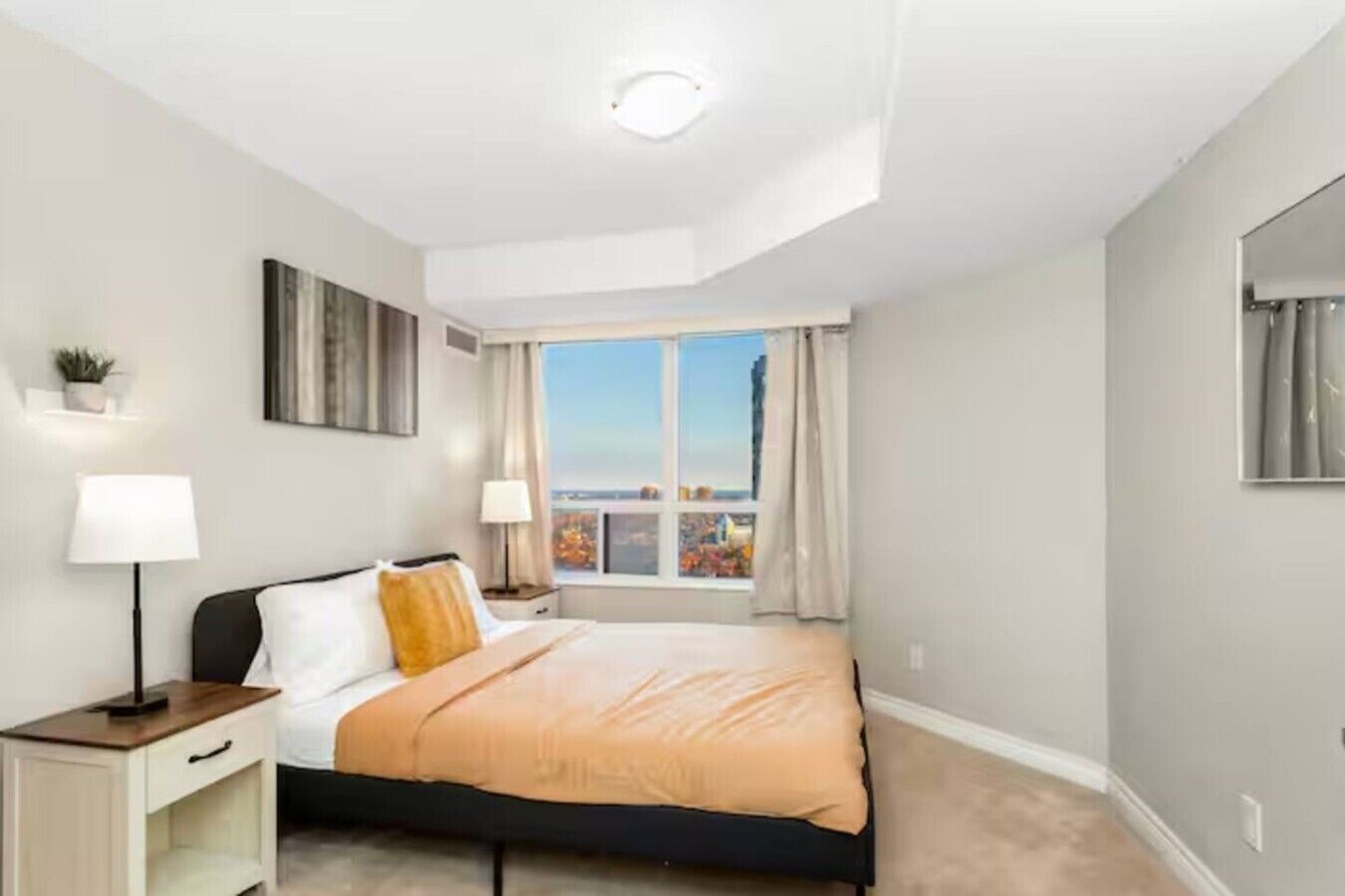 Ein Hotelzimmer mit Bett, Nachttischlampen, einem Nachttisch, einem Fenster mit Vorhängen und Blick auf die Stadtlandschaft.