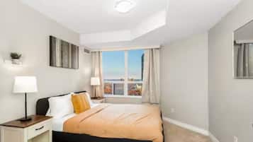 A hotel room with a bed, bedside lamps, a nightstand, a window with curtains, and a view of the cityscape.
