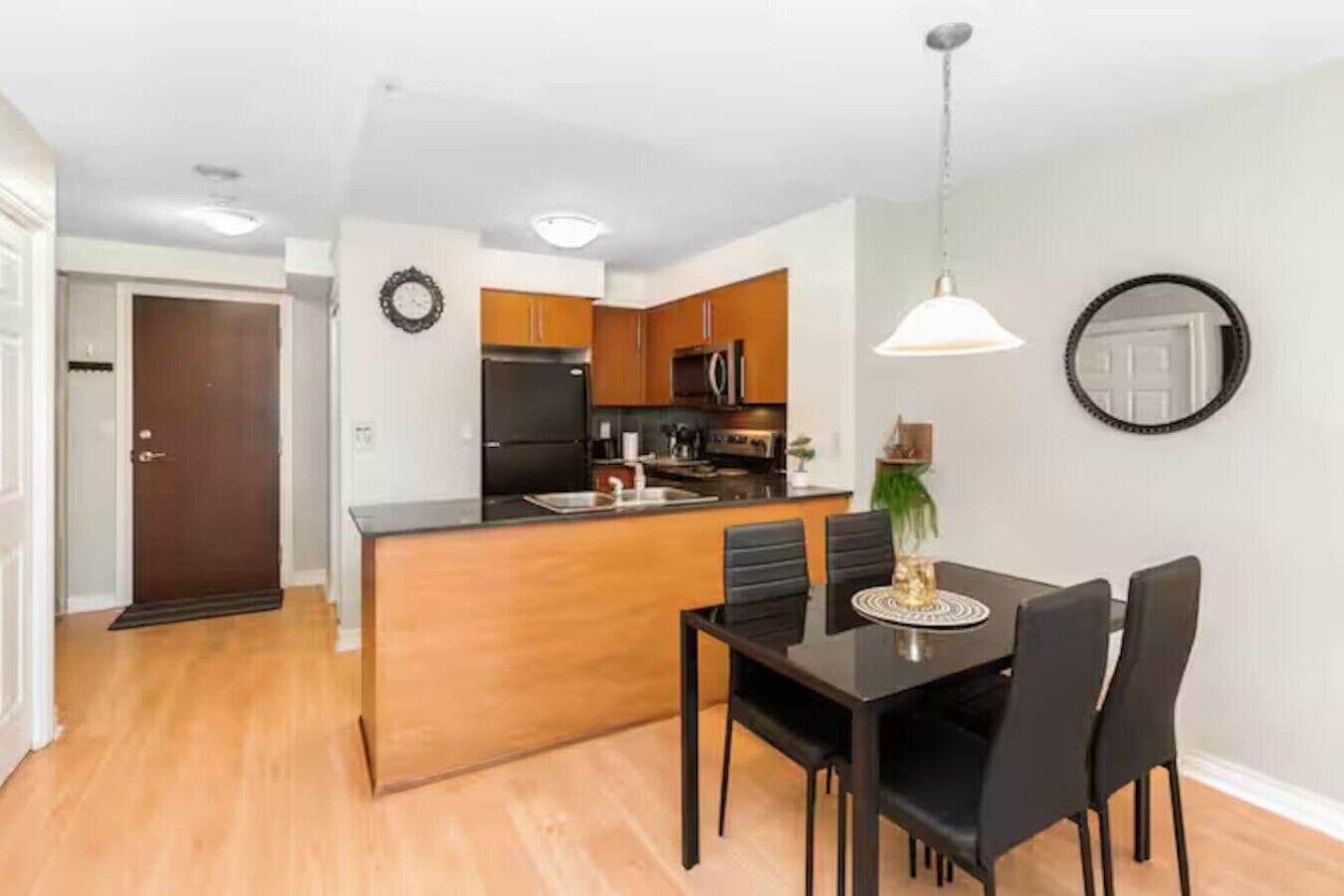 A modern kitchen with wooden cabinets, a black refrigerator, and a dining area with a black table and chairs.