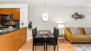 Een moderne keuken met een magnetron, fornuis en spoelbak, een eethoek met een tafel en stoelen, een bank en een hanglamp.