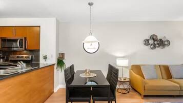 Een moderne keuken met een magnetron, fornuis en spoelbak, een eethoek met een tafel en stoelen, een bank en een hanglamp.