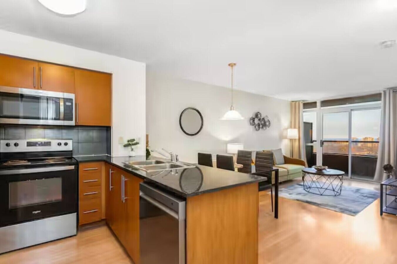 A modern kitchen with a built-in oven and microwave, a dining area with a round table, and a view through a large sliding glass door.