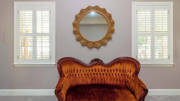 A room with a large mirror, two windows with shutters, and a plush upholstered chair. - Midland Poolside Family Oasis (Columbus)