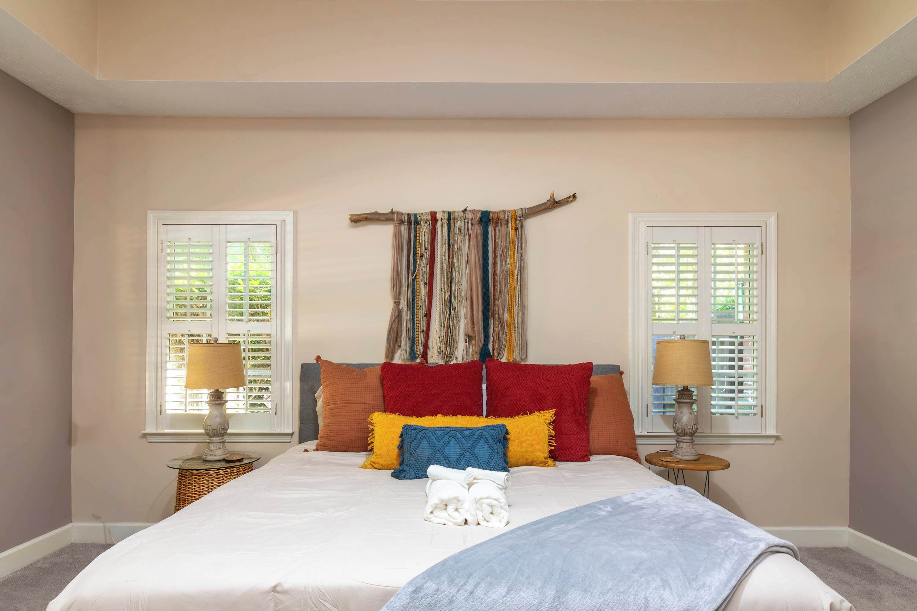 Une chambre avec un grand lit, deux tables de chevet, une fenêtre avec des volets et un rideau fixé au mur.