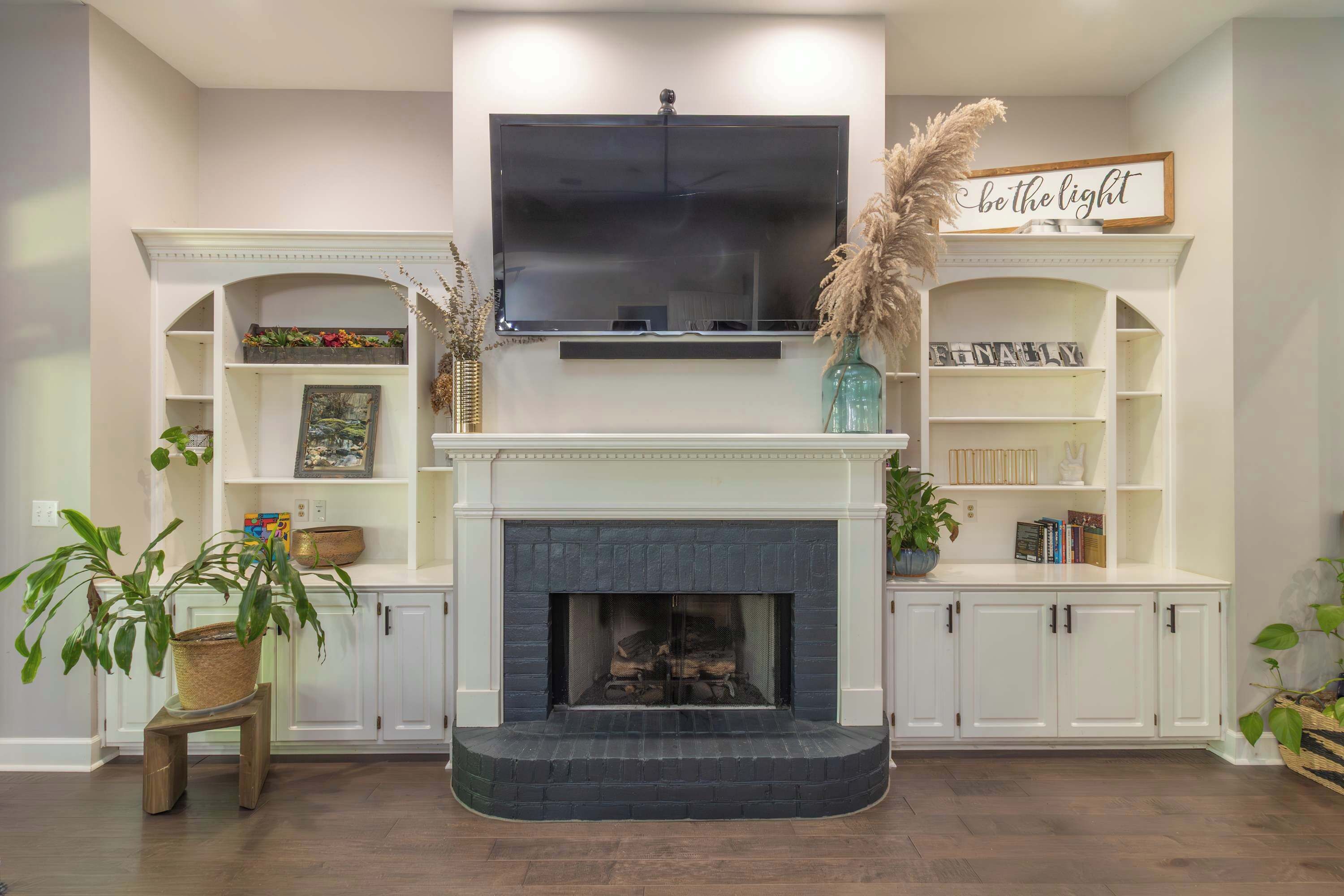 Una sala de estar con chimenea, televisor montado y estanterías empotradas decoradas con objetos.
