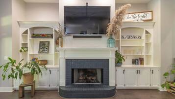 Una sala de estar con chimenea, televisor montado y estanterías empotradas decoradas con objetos.