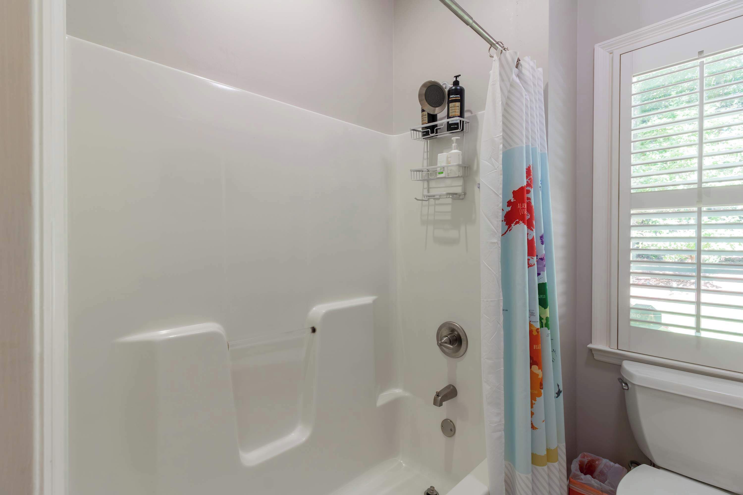A bathroom with a white bathtub, a shower curtain with a map design, and a window with blinds.