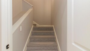 A carpeted staircase with a white handrail and a light switch on the wall. - Midland Poolside Family Oasis (Columbus)