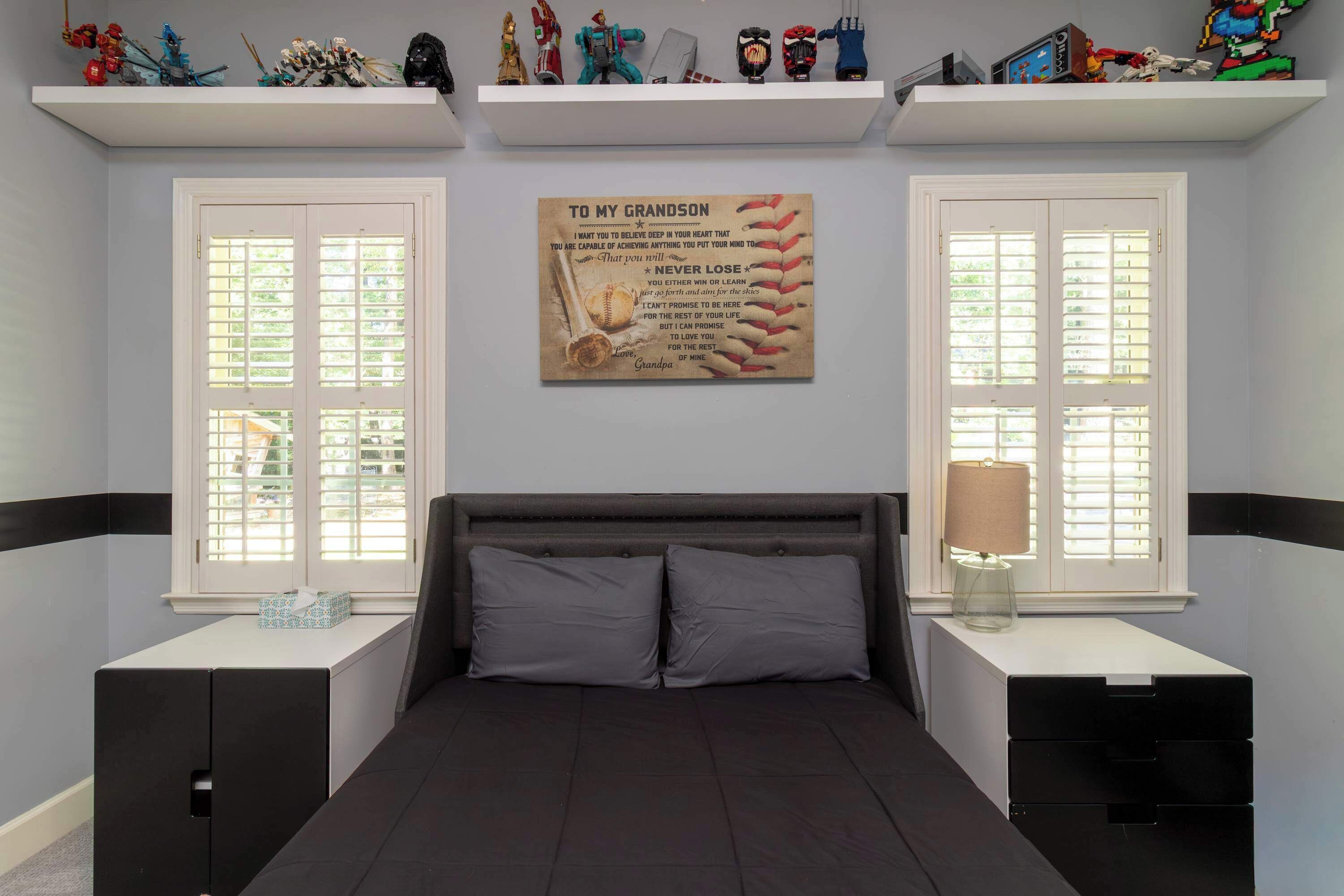A bedroom with a bed, two nightstands, a wall-mounted shelf with toys, and a motivational poster.