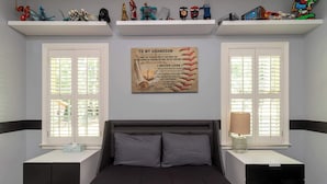 A bedroom with a bed, two nightstands, a wall-mounted shelf with toys, and a motivational poster. - Midland Poolside Family Oasis (Columbus)