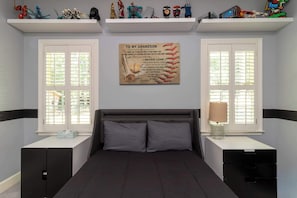 A bedroom with a bed, two nightstands, a wall-mounted shelf with toys, and a motivational poster.