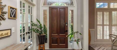 A hallway with a wooden bench, a potted plant, a rug, and a door with a window above it.