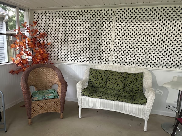 A wicker chair with a green cushion and a white wicker chair with a patterned cushion.