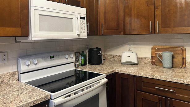 A kitchen with wooden cabinets, a white microwave, a stove, and a toaster. - Comfortable Charming Convenient in Covington TN (Covington)