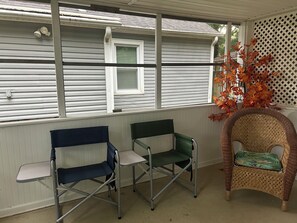 A covered porch with two folding chairs and a wicker chair.