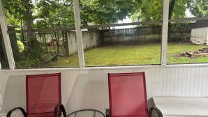 A covered patio with two red chairs and a small table, overlooking a backyard with a wooden fence and grass. - Comfortable Charming Convenient in Covington TN (Covington)