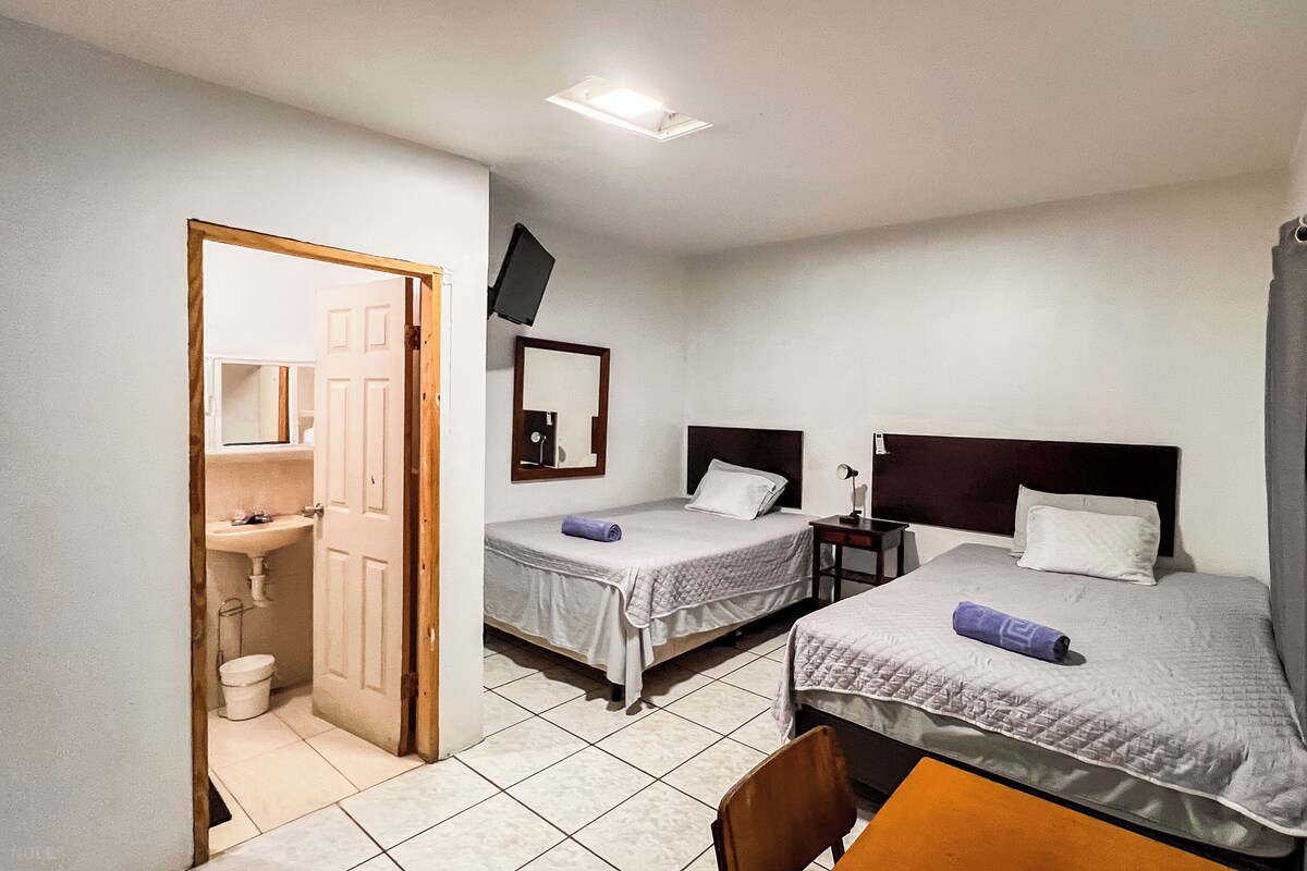 A hotel room with two beds, a bathroom, a desk, and a chair.