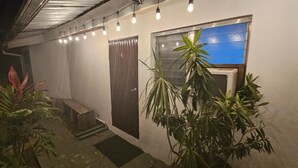 Un pasillo estrecho con una puerta, una ventana con persianas y plantas en macetas.